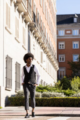 Afro boy dressed in suit and sunglasses crossing the crosswalk in the middle of the city. Vertical photo