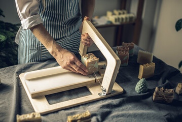 Women's hands cut homemade natural soap on a professional wood cutter. A means of eco-friendly...