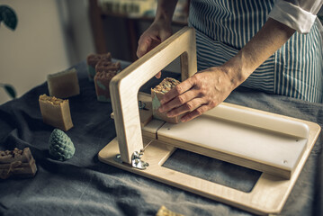 Women's hands cut homemade natural soap on a professional wood cutter. A means of eco-friendly hygiene