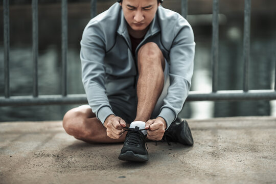 A man tying shoelaces on sport shoes in the city center park before cardio workout, running. Health and Lifestyle in big city life concept. - Powered by Adobe