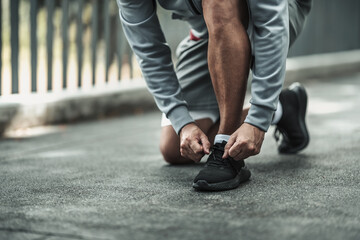 A man tying shoelaces on sport shoes in the city center park before cardio workout, running. ...