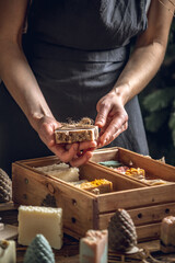 A woman soap maker holds handmade soap in her hands. A lot of different sliced pieces in a wooden box. Eco-friendly natural handmade cosmetics