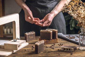 Women's hands cut coffee homemade natural soap on a professional wood cutter. A means of...