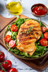 Grilled chicken breast with arugula and tomatoes on a plate vertical photo