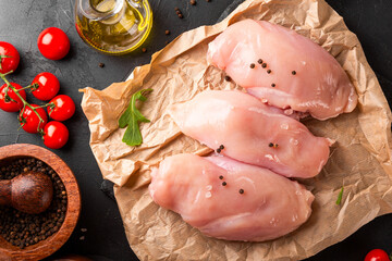Raw chicken breast meat and spices for its preparation on a black background, top view