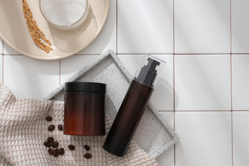 Against the white tiles background, set of bottle product for skin care and hair care displayed on marble tray with coffee beans and towel. Top view, mockup bottle unlabeled for design