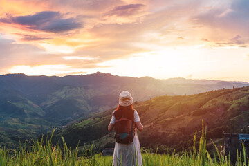 Happy young woman traveler relaxing and looking at the beautiful sunrise on the top of mountains, Travel lifestyle concept