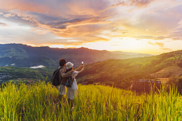 Happy young couple traveler relaxing and looking at the beautiful sunrise on the top of mountains,...
