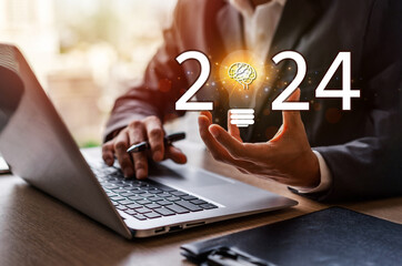 Business people using laptop computer and holding light bulb for success business with 2024 new...