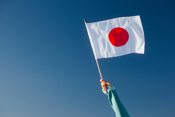 Hand Waiving a Japanese Flag on a Blue Sky. Cheerful enthusiastic patriotic person displaying the...