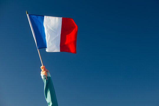 Hand Waiving an French Flag on a Blue Sky. Cheerful enthusiastic patriotic person displaying the symbol of France
