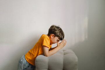 A boy in an orange T-shirt prays at home. Reading the Holy Bible. Concept for faith, spirituality and religion. Peace, hope.