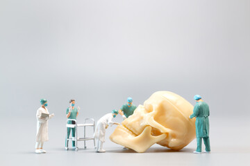 Miniature people Doctor with a giant human skull on a grey background