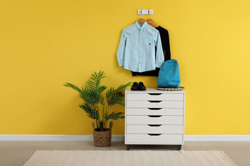 Stylish school uniform hanging on yellow wall with chest of drawers in room