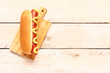 Board with tasty hot dog on white wooden background
