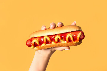Woman holding tasty hot dog on yellow background - obrazy, fototapety, plakaty