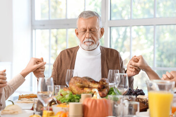 Happy family praying before dinner at festive table on Thanksgiving Day