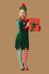 Young woman in elf costume holding Christmas gift box on brown background