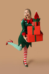 Young woman in elf costume holding Christmas gift boxes on brown background