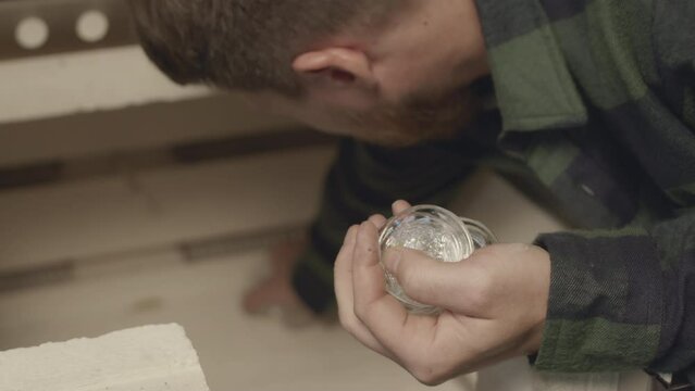 Medium closeup with slowmo of professional male gaffer taking out cooled down small glass pieces out of glass making oven while working at manufacturing factory