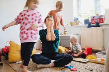 Stressed out mother sitting on floor while children running around her.