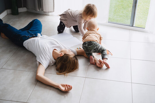 Tired mother lying on floor while her children drawing nearby.
