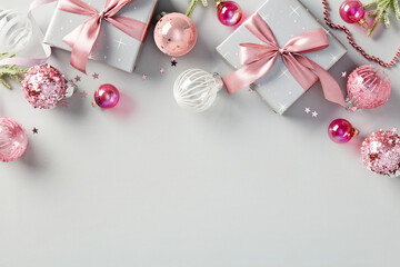 Gift boxes adorned with pink ribbon, shiny balls, and festive fir branches create a stylish and...