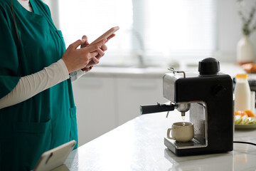 Cropped image of nurse checking social media on smartphone when making morning coffee
