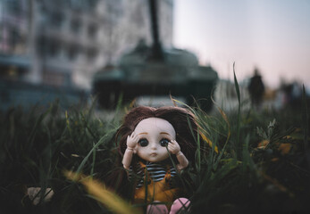 the concept of destroying childhood by war. frightened doll against the background of a tank and a...