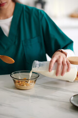 Cropped image of medical nurse adding non-dairy milk in bowl with muesli