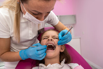 cute little girl sits on a dental chair and treats aching teeth, makes a face.