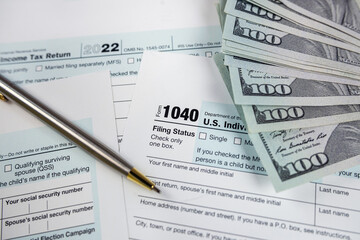 Income tax return 1040 forms with blue pen and us dollar bills at office desk