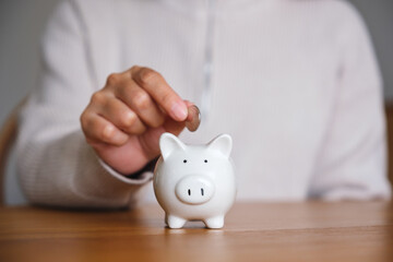 Closeup image of a woman putting coins into piggy bank for saving money concept - obrazy, fototapety, plakaty