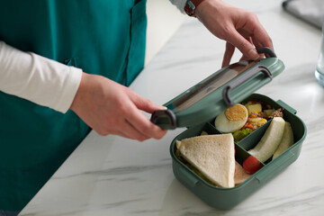 Hands of medical nurse closing lunch box with prepared sandwiches and salad