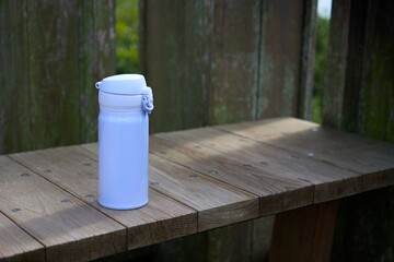 屋外で木のベンチに置かれた水色の水筒