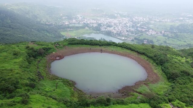Cinematic aerial view of the sacred lake at the Brahmagiri hill in the Western Ghats of Maharashtra during monsoon with the view of Trimbak town in the background, Nashik, India