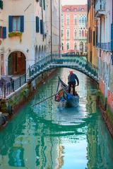 Papier Peint photo Gondoles Venetian gondolier punting gondola through green canal waters of Venice Italy