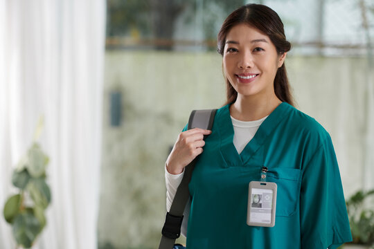 Portrait of smiling Vietnamese medical intern in scrubs standing in her apartment
