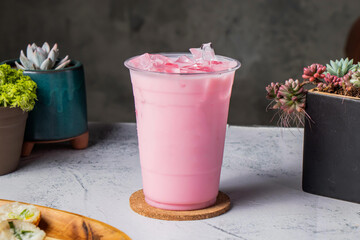 iced strawberry milk or rose milk served in disposable glass with ice cube isolated on wooden board...