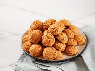 Plate of cookie amaretti on white marble background - traditional Italian Sardinian pastry. Delicious amaretti biscuit cookies made from almond or apricot kernels with copy space