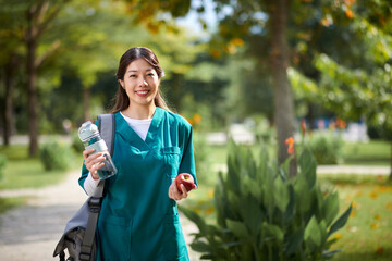Portrait of cheerful medical nurse spending lunch time in park, having fresh apple and water