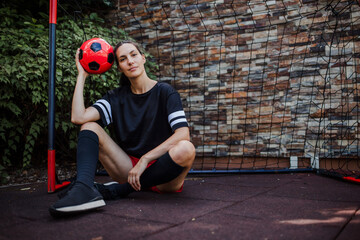 Beautiful female football player standing by football goal with ball in her hand. The woman plays...