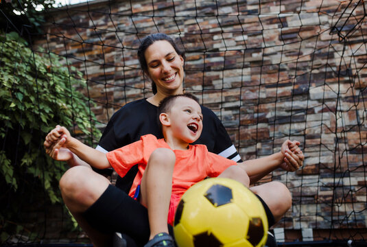 Mom playing football with her son, dressed in football jerseys. The family as one soccer team. Family sports activities outside in the backyard or on the street.