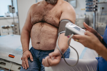 Female doctor measuring blood pressure, examining hypertension, using blood pressure monitor. Obesity affecting middle-aged men's health. Concept of health risks of overwight and obesity.