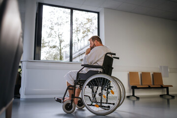 Side view of man in wheelchair. Overweight patient in hospital gown waiting for medical examination...