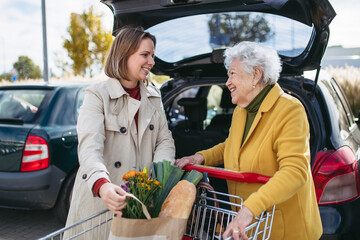 Mature granddaughter helping grandmother load groceries in to the car. Senior woman shopping at the...