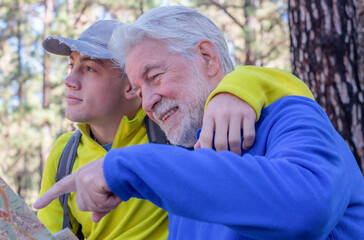 Young grandson and old grandfather consulting trail map while hiking in mountain forest enjoying...