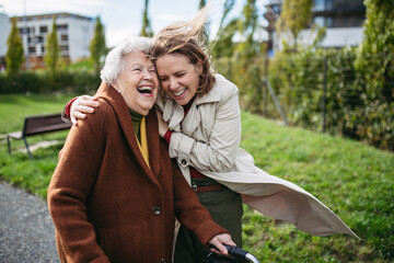 Grandmother and mature granddaughter on a walk in city park, during windy autumn day. Caregiver and...