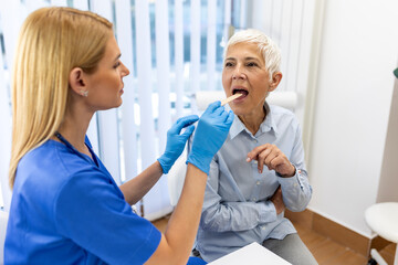 Senior patient opening her mouth for the doctor to look in her throat. Female doctor examining sore...