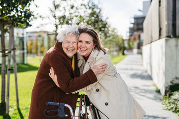 Grandmother and mature granddaughter on a walk in city park, during windy autumn day. Caregiver and...